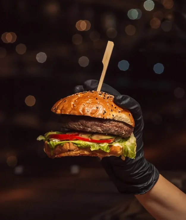 A burger held in a black-gloved hand
